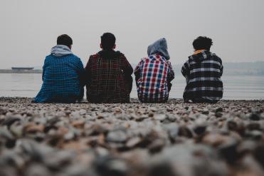 Vier Teenager sitzen mit dem Rücken zur Kamera am Ufer
