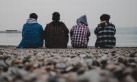 Vier Teenager sitzen mit dem Rücken zur Kamera am Ufer